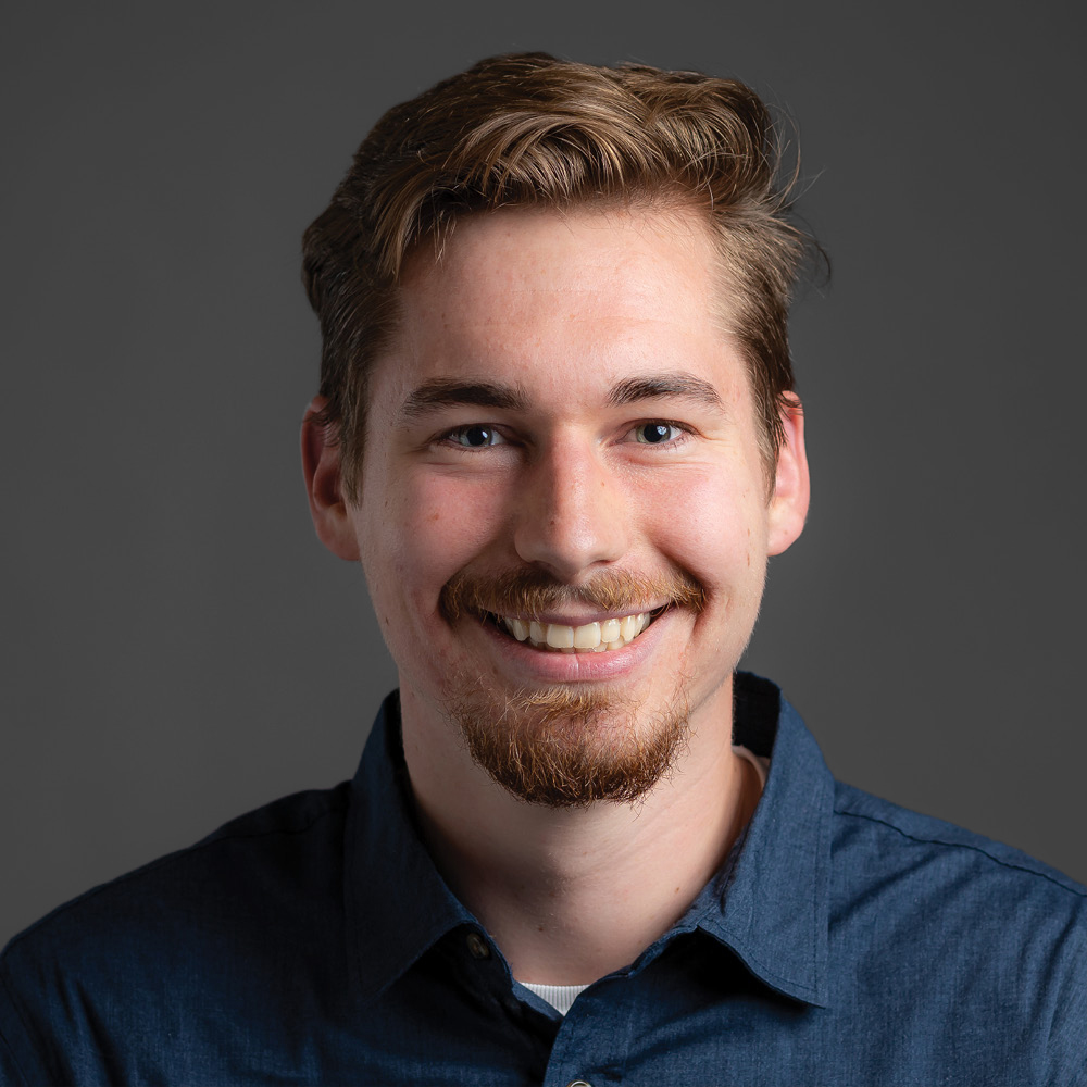 Lawson Doden smiling wearing a blue dress shirt in front of a dark grey background