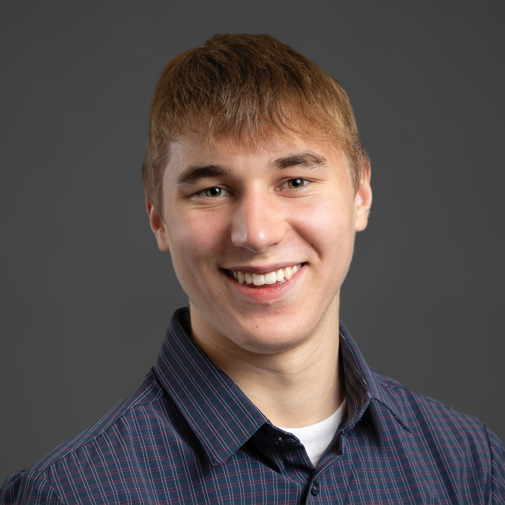 Jones Doden smiling and wearing a blue shirt on a dark grey background