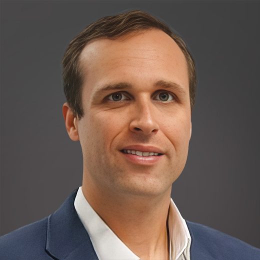Professional headshot of a man in a navy blazer and open-collar white shirt against a dark gray background.